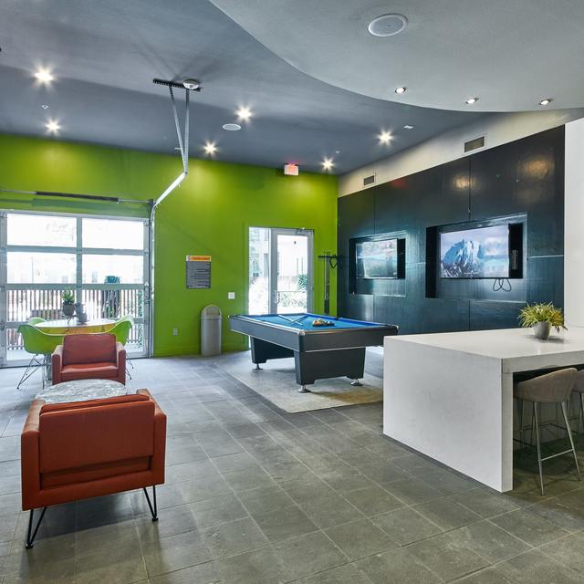 Interior of the clubhouse with lounge seating, a pool table, televisions, and a retractable garage door to the outside