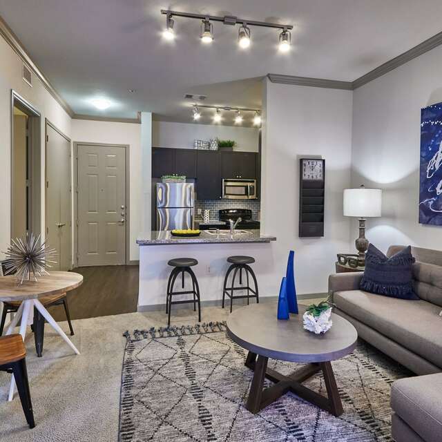 Living room with carpet flooring, a grey sectional, and blue artwork on the walls