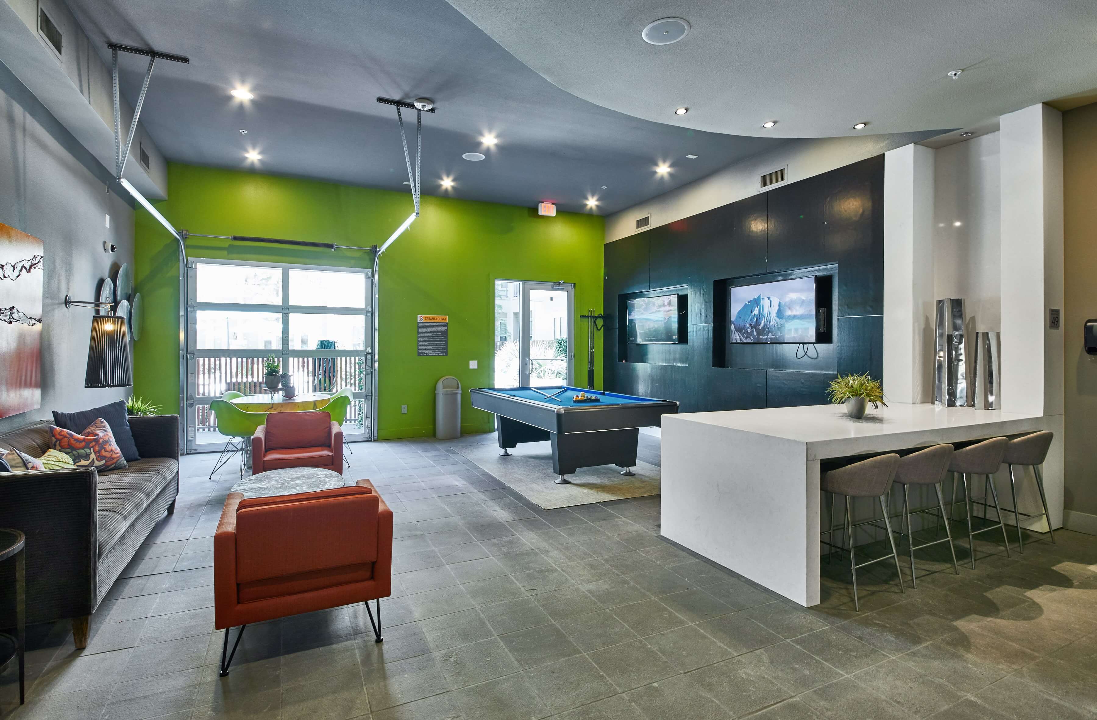 Interior of the clubhouse with lounge seating, a pool table, televisions, and a retractable garage door to the outside