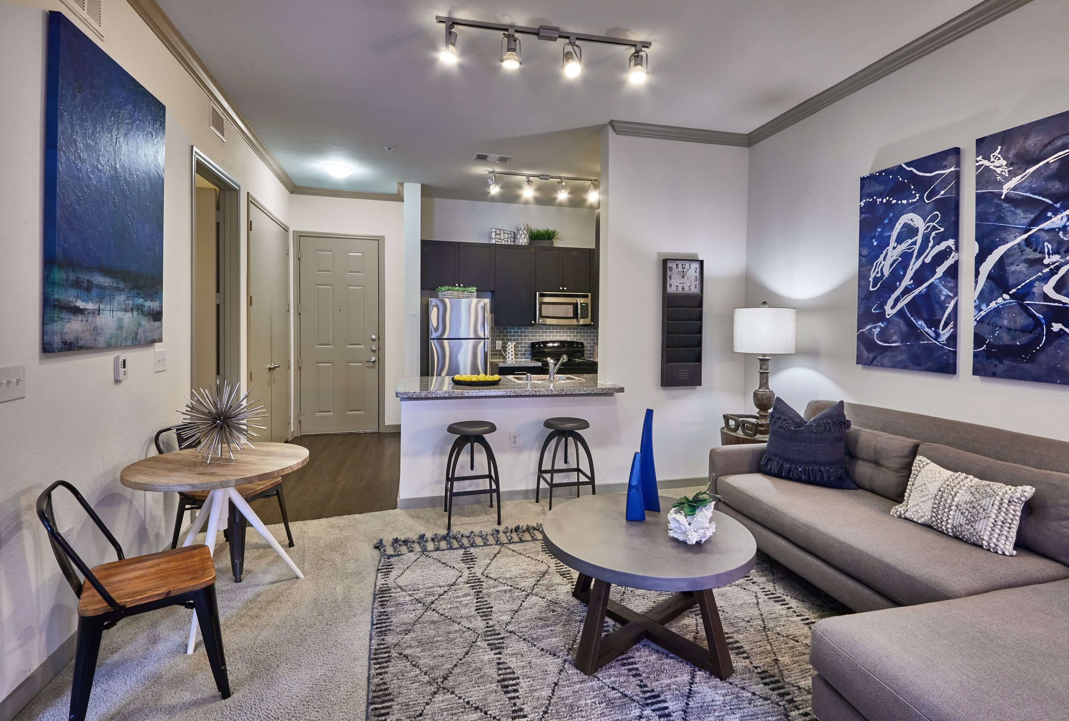 Living room with carpet flooring, a grey sectional, and blue artwork on the walls