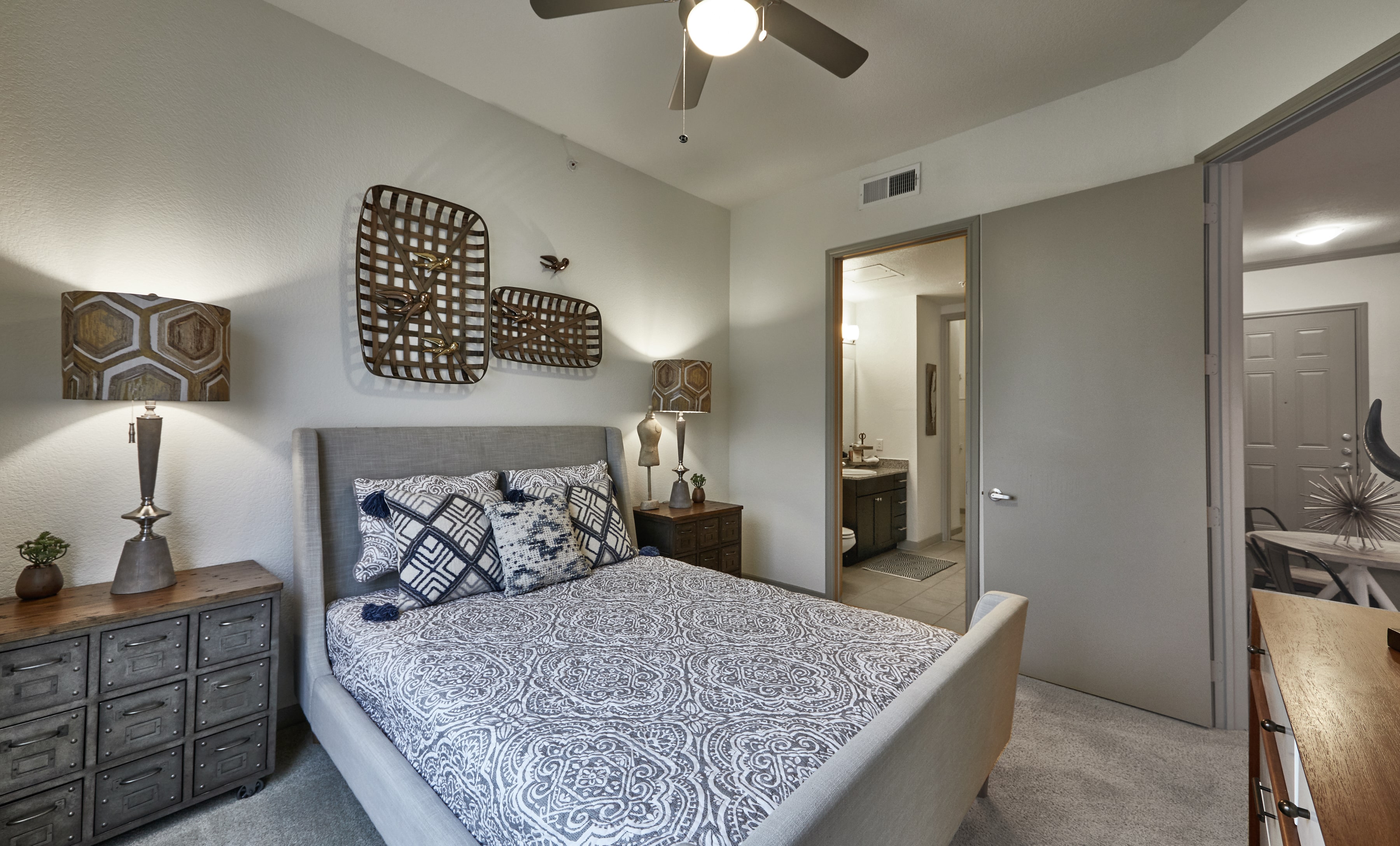 Primary bedroom suite with a grey fabric bed, nightstands, and a ceiling fan